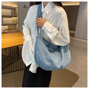 Detail of light blue denim hobo bag with wide shoulder strap and silver metal button