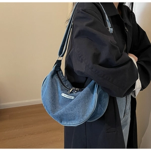 Detail of blue denim crescent bag showing adjustable strap and white woven logo tag