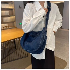Detail of dark blue denim messenger bag with white stitching worn by a model