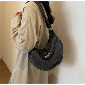 Close-up of a dark grey denim crescent bag featuring a white fashion woven label