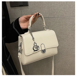 Detailaufnahme der cremeweißen Handtasche mit Lederstruktur, Silberbeschlägen und Metallanhänger