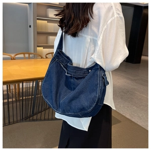 Detail view of a dark blue denim hobo messenger bag with white stitching and side pocket