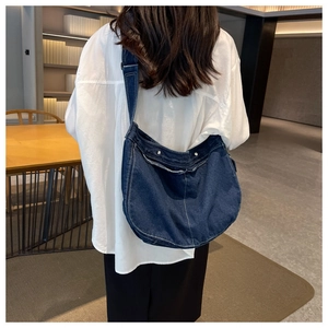 Detail of dark blue denim messenger bag with white stitching and silver button
