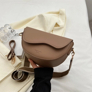Vintage brown saddle bag with wave flap and wide fabric strap in minimalist setting