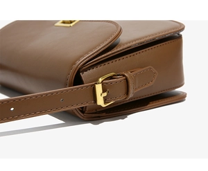 Detail of the golden metal buckle and fine stitching on a brown leather crossbody bag