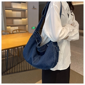 Detail view of a large blue denim hobo bag with white stitching and wide shoulder strap
