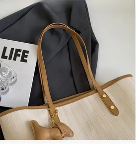 Detail of off-white tote bag with wave texture, brown handles and dog-shaped leather charm