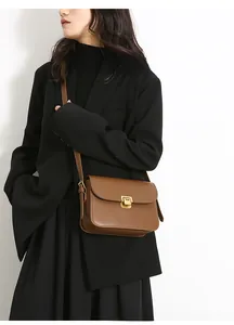 Detail of vintage caramel leather crossbody bag with elegant gold clasp on black blazer