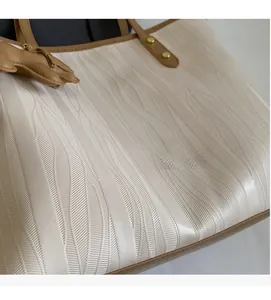 Detailed view of beige tote bag featuring wavy texture and brown leather accents