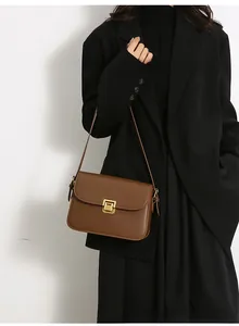 Detail view of brown leather shoulder bag with golden buckle on a black blazer model