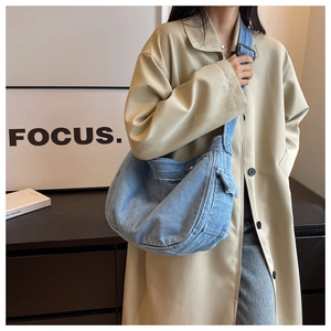 Detail view of a light blue denim crescent messenger bag styled with a khaki trench coat