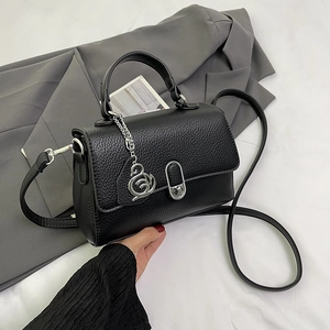 Schwarze Handtasche mit Litschi-Maserung und Schwan-Anhänger auf grauem Blazer