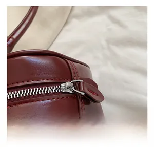 Close-up of shiny burgundy leather texture with silver metal zipper and red stitching