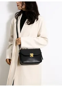 Detail of a chic black crossbody bag with gold lock closure shown on a beige coat