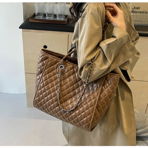 Brown quilted tote bag with chain strap styled with a trench coat in a cozy room