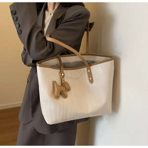Detail of cream and brown tote bag featuring wavy texture and cute dog charm on model