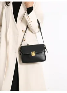 Detail of black glossy leather square crossbody bag with gold buckle on white coat