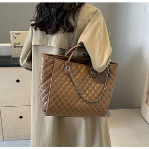 Detailed view of brown quilted tote bag with silver chain straps worn with a trench coat