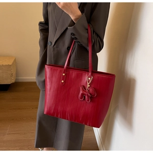 Detail of red ripple texture tote bag with a dog-shaped charm and slender handles