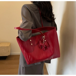Detail of dark red leather tote bag with vertical texture and red dog charm