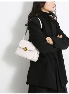 Detail of elegant cream-colored flap crossbody bag with golden square lock on a black coat