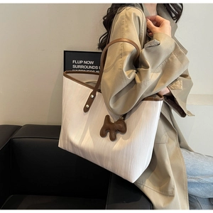 Detail of white wavy textured tote bag with brown leather handles and puppy charm