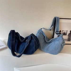 Blue denim messenger hobo bag with wide adjustable strap shown in minimalist studio setting