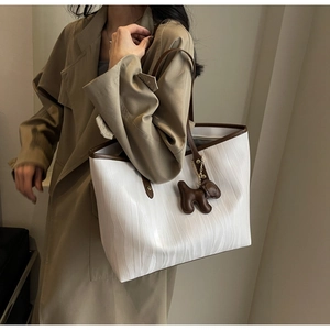 Detail of white wave-textured tote bag with brown contrast trim and dog charm pendant