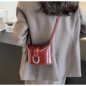 Detailed close-up of a burgundy glossy leather crossbody bag with silver U-shaped buckle