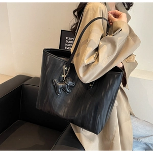 Detail of black tote bag with wave texture and cute dog charm displayed by model