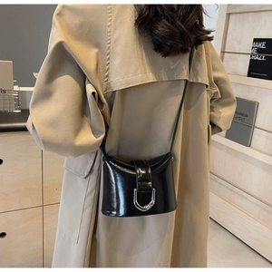 Detail of a black glossy leather bucket bag with silver D-ring buckle on a shoulder strap
