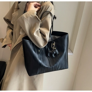 Black tote bag with wood grain texture and dog charm shown on a model's shoulder