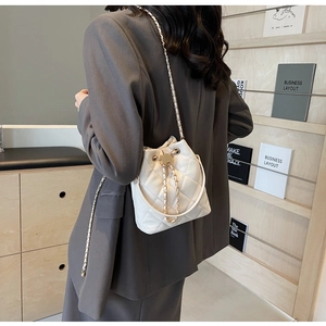 Detail of cream quilted bucket bag with gold ring hardware and chain strap on shelf