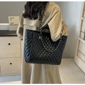 Close-up of black quilted tote bag with chain strap worn with a beige autumn coat