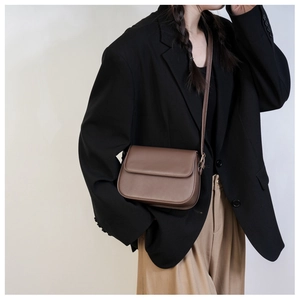 Détail d'un sac bandoulière minimaliste en cuir marron foncé porté par un modèle