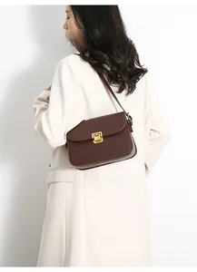 Detail of model wearing a dark brown leather crossbody bag with golden metal clasp