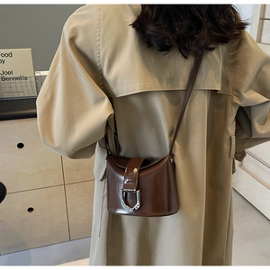 Rear view of model wearing a brown glossy leather bucket bag with silver U-shaped buckle