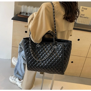 Quilted black tote bag with silver chain straps shown on shoulder in lifestyle scene