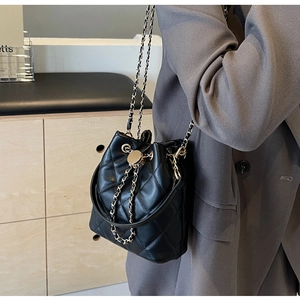 Close-up of black quilted bucket bag with gold lock and chain strap on a blazer
