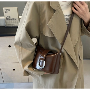 Detail of dark brown leather bucket bag with silver U-shaped buckle on a beige trench coat