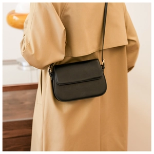 Vue détaillée d'un sac bandoulière en cuir noir porté avec un trench-coat classique kaki