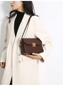 Detail of dark brown leather crossbody bag featuring a gold square clasp and accordion sides