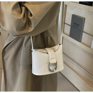 Detail of minimalist cream crossbody bucket bag with a silver D-ring buckle on trench coat