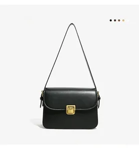 Detail of minimalist black leather crossbody bag featuring a classic gold metal lock