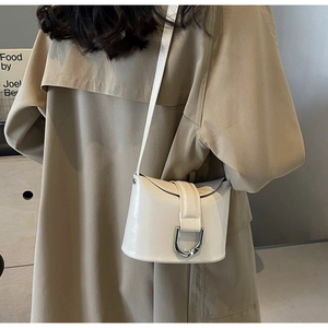 Detail of a creamy white patent leather bucket bag featuring a large silver D-buckle