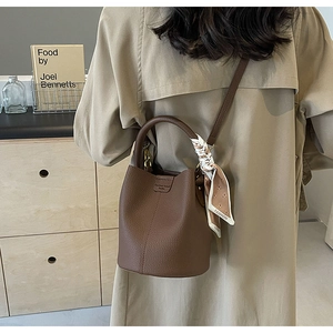 Detail of a brown pebble leather bucket bag with a silk scarf tied on the handle