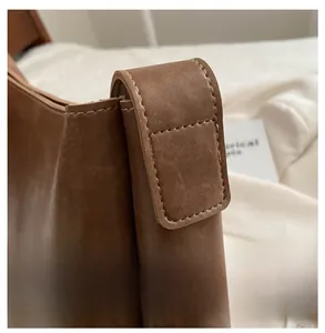 Gros plan des coutures renforcées sur la bandoulière du sac seau vintage en cuir marron