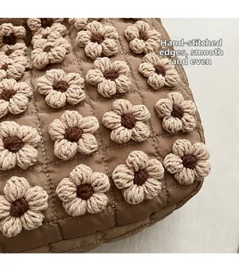 Detail of warm brown quilted handbag with white stitching and handmade crochet flowers