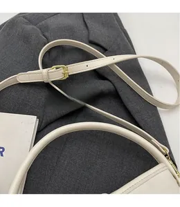 Close-up of cream bucket bag with adjustable shoulder strap and gold buckle detail