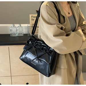 Detail of a black leather shoulder bag with double bow decoration on a khaki trench coat